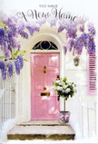 The scene shows a sunlit entrance that feels like it could belong to a newly settled family in Mitcham, perhaps near the leafy paths leading to Figges Marsh. A softly coloured pink door anchors the composition, its pastel shade lending a tender warmth to the otherwise simple façade. Around and above the door, wisteria vines tumble generously, their drooping racemes of lavender, lilac, and soft purple blossoms hanging like fragrant garlands. Each cluster is made up of many small petals, which catch the light in varying degrees, creating a sense of depth and gentle motion as if the blooms might rustle softly at the touch of a breeze. The whitewashed wall provides a calm, luminous backdrop, subtly textured and touched here and there by shadows from the overhead flowers. At ground level, placed right at the doorstep, sits a grey metal bucket that has been transformed into a symbol of welcome. It brims with white and creamy roses, their petals folded into lush rosettes, some fully open, others still just unfurling. Wisps of fresh green foliage weave through the arrangement, adding a hint of natural wildness within the otherwise classic composition. A soft pink ribbon is tied round the bucket's base, its bow loose and graceful, lightly pooling on the stone. The overall feeling is one of gentle joy and expectation, as if these flowers were arranged to greet someone arriving at their new Mitcham address, offering a blend of elegance, comfort, and quiet celebration each time they step over the threshold.